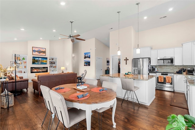 dining area featuring a glass covered fireplace, dark wood-type flooring, a ceiling fan, and high vaulted ceiling