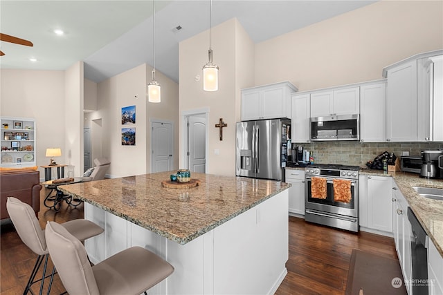 kitchen with light stone counters, dark wood finished floors, decorative backsplash, appliances with stainless steel finishes, and white cabinetry