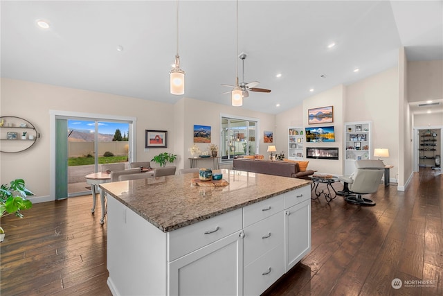 kitchen with light stone counters, a center island, a glass covered fireplace, and dark wood-style flooring