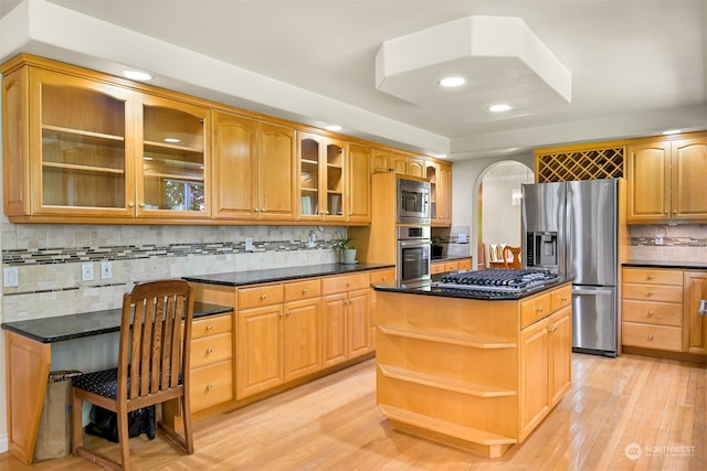 kitchen with light wood-type flooring, a center island, decorative backsplash, appliances with stainless steel finishes, and dark stone countertops