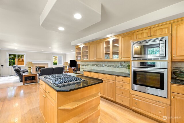 kitchen with a kitchen island, light hardwood / wood-style flooring, appliances with stainless steel finishes, dark stone countertops, and decorative backsplash