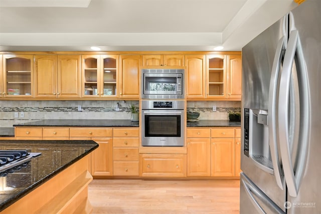 kitchen featuring dark stone counters, backsplash, appliances with stainless steel finishes, and light hardwood / wood-style flooring