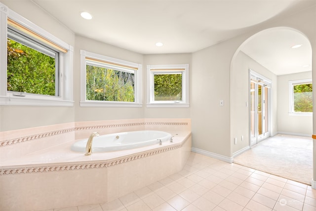 bathroom with a relaxing tiled tub, plenty of natural light, and tile patterned floors