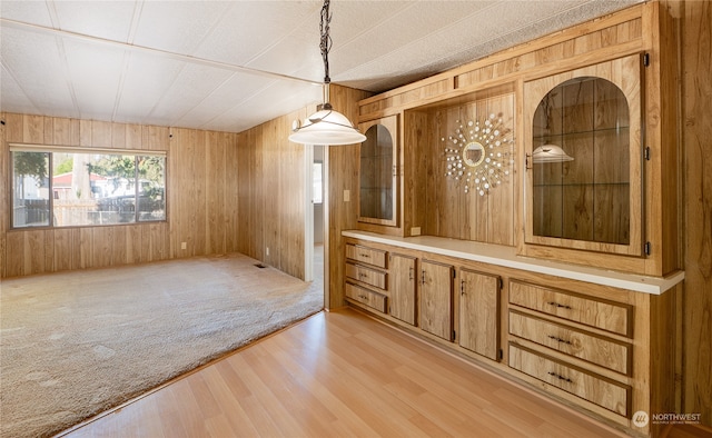 unfurnished dining area with a textured ceiling, wooden walls, and light hardwood / wood-style floors