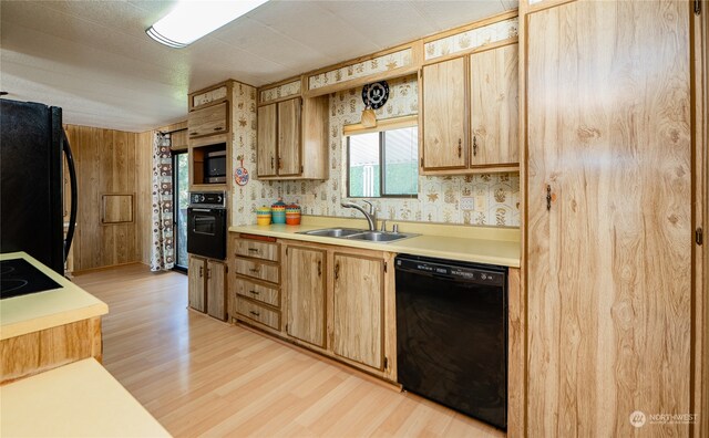 kitchen featuring light hardwood / wood-style flooring, wooden walls, black appliances, and sink