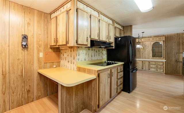 kitchen featuring hanging light fixtures, kitchen peninsula, wood walls, light wood-type flooring, and black appliances