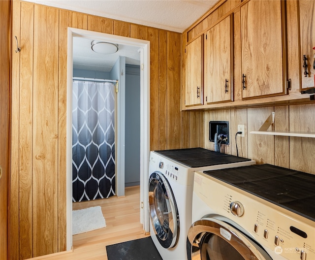 washroom featuring cabinets, light wood-type flooring, wood walls, and washer and clothes dryer