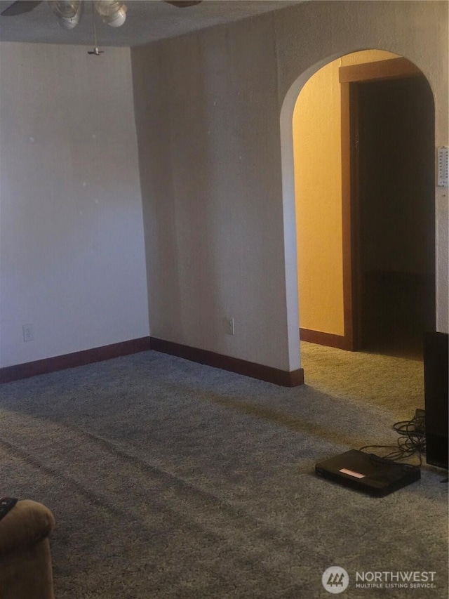 empty room with arched walkways, carpet, a ceiling fan, and baseboards