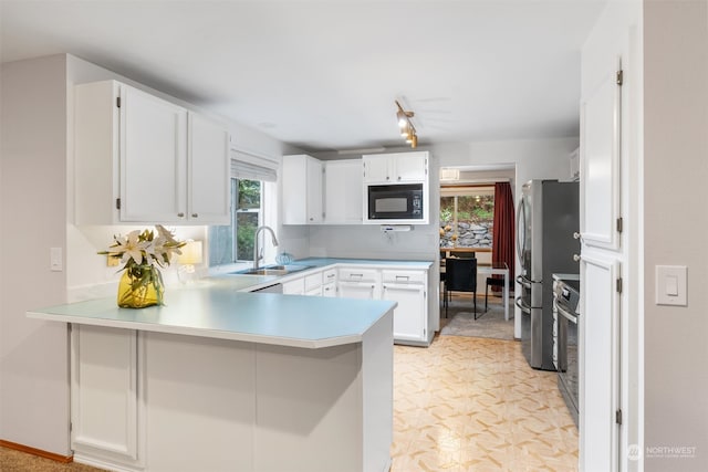 kitchen with white cabinets, sink, kitchen peninsula, track lighting, and stainless steel appliances