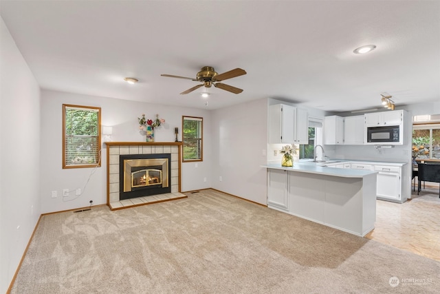 kitchen with a wealth of natural light, kitchen peninsula, black microwave, and white cabinetry