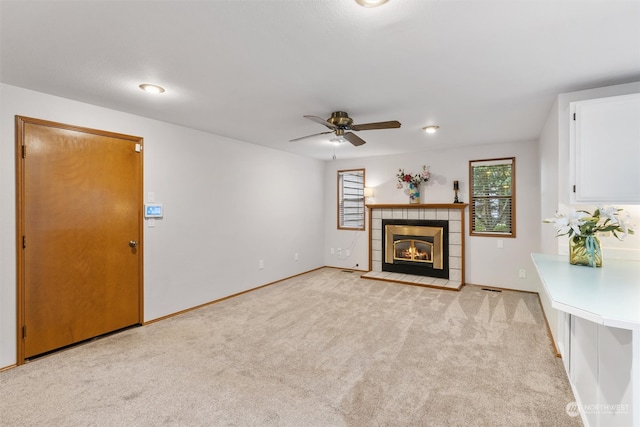 unfurnished living room with a tile fireplace, light carpet, and ceiling fan