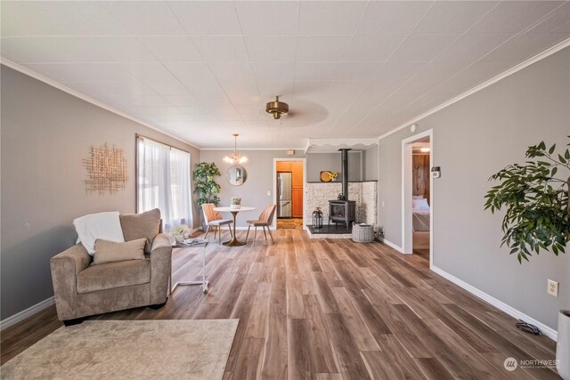 living room with ornamental molding, a wood stove, ceiling fan with notable chandelier, and hardwood / wood-style floors