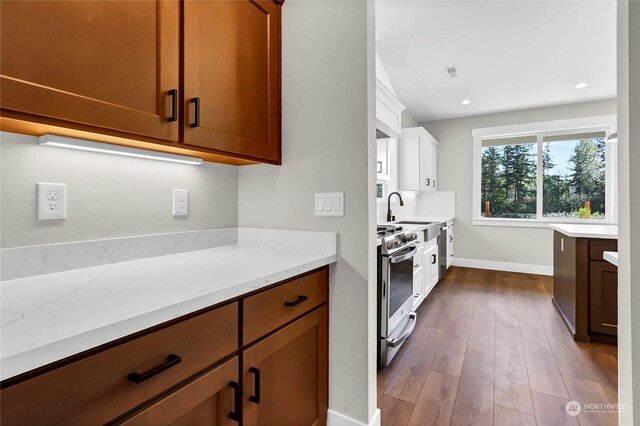 kitchen with stainless steel appliances, wood-type flooring, light stone countertops, and sink