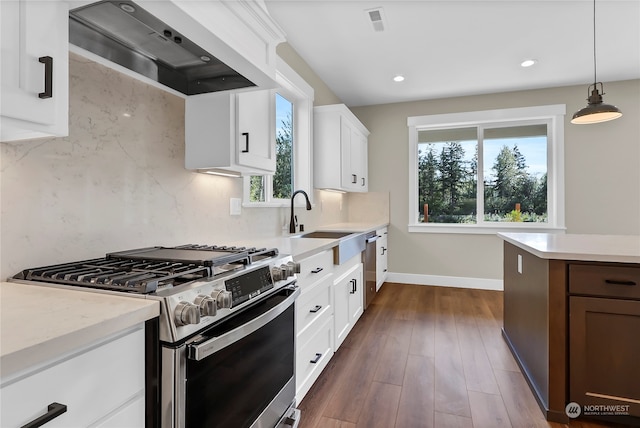 kitchen featuring dark hardwood / wood-style floors, stainless steel gas stove, sink, wall chimney range hood, and hanging light fixtures