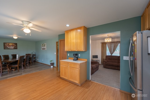 kitchen featuring stainless steel refrigerator, light wood-type flooring, pendant lighting, light brown cabinetry, and ceiling fan with notable chandelier