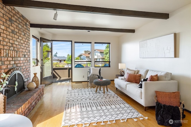 living room featuring a brick fireplace, beamed ceiling, light hardwood / wood-style floors, and a wealth of natural light