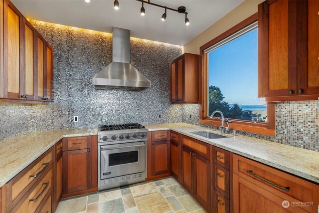 kitchen featuring premium range, sink, tasteful backsplash, wall chimney exhaust hood, and light stone countertops