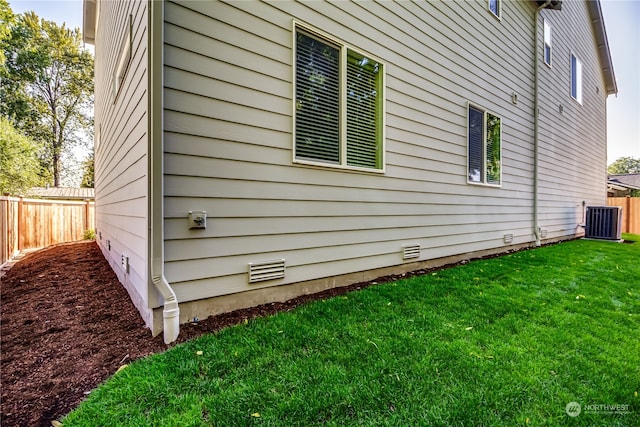 view of side of home with central AC unit and a yard