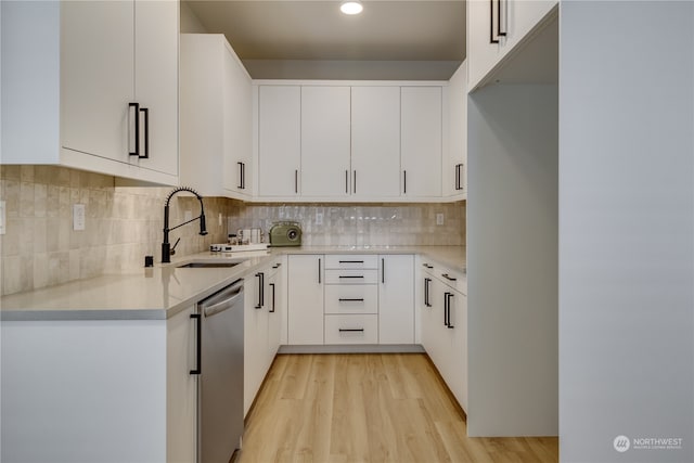 kitchen featuring white cabinets, sink, tasteful backsplash, stainless steel dishwasher, and light wood-type flooring