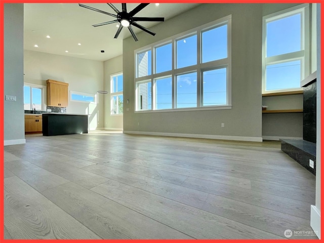 unfurnished living room with light hardwood / wood-style floors, a healthy amount of sunlight, a towering ceiling, and ceiling fan