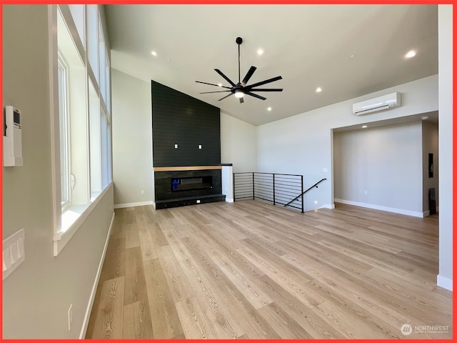 unfurnished living room featuring vaulted ceiling, a wall mounted AC, light hardwood / wood-style flooring, and ceiling fan