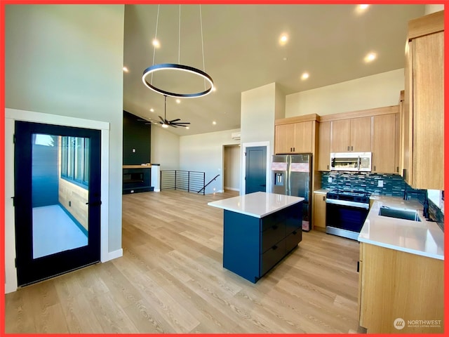 kitchen with appliances with stainless steel finishes, a center island, hanging light fixtures, light hardwood / wood-style flooring, and light brown cabinets