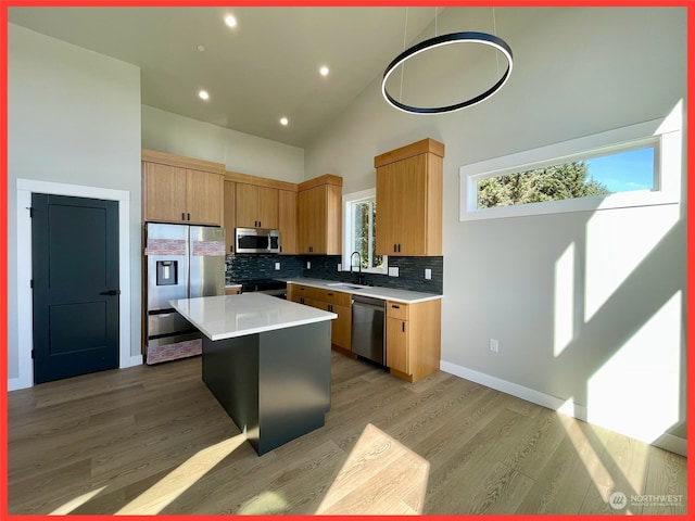 kitchen with appliances with stainless steel finishes, a center island, light hardwood / wood-style floors, pendant lighting, and high vaulted ceiling