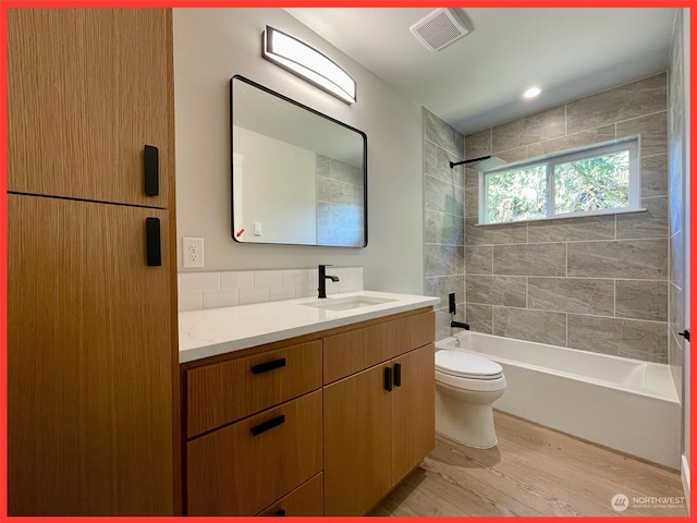 full bathroom with tiled shower / bath, vanity, hardwood / wood-style flooring, and toilet