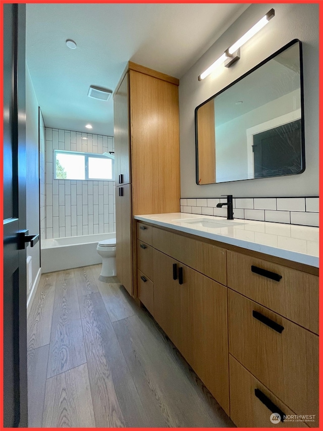 full bathroom with tasteful backsplash, toilet, tiled shower / bath, vanity, and hardwood / wood-style flooring