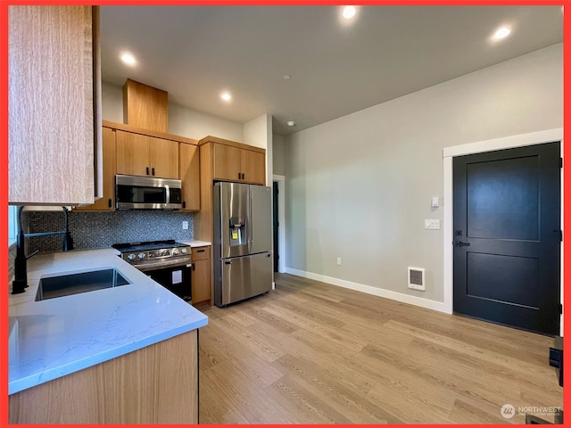 kitchen featuring decorative backsplash, light stone countertops, light wood-type flooring, sink, and stainless steel appliances