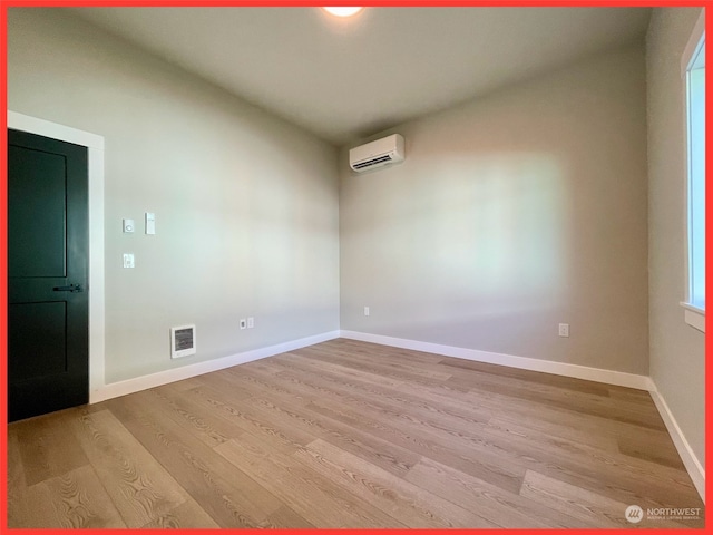 spare room featuring a wall mounted AC and light wood-type flooring