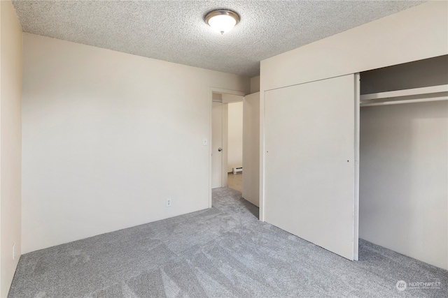 unfurnished bedroom featuring light carpet, a baseboard heating unit, a closet, and a textured ceiling