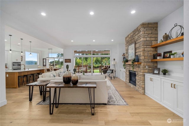 living room featuring a stone fireplace, light wood-type flooring, and sink