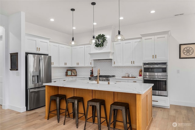 kitchen featuring a center island with sink, light hardwood / wood-style floors, stainless steel appliances, and white cabinets