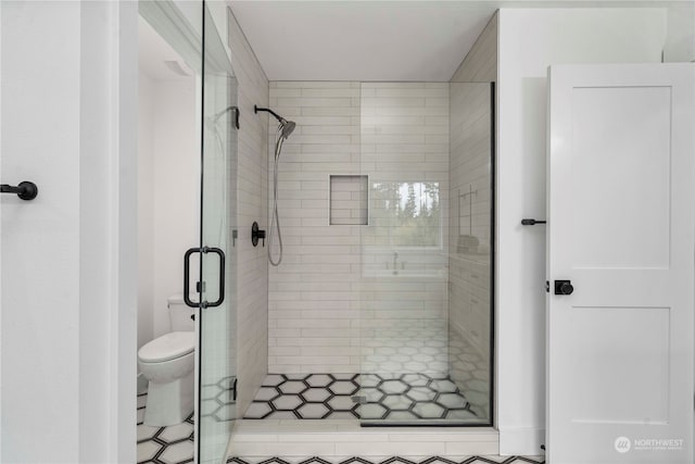 bathroom featuring a shower with door and toilet