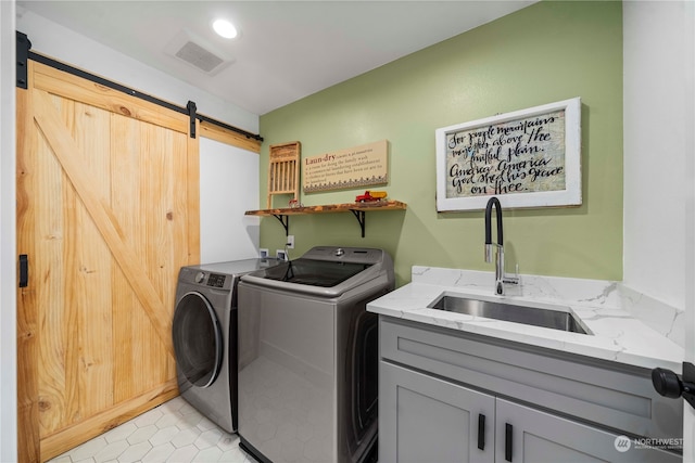 clothes washing area with light tile patterned floors, sink, cabinets, separate washer and dryer, and a barn door