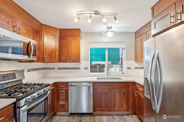 kitchen with sink, backsplash, appliances with stainless steel finishes, light stone countertops, and light hardwood / wood-style floors