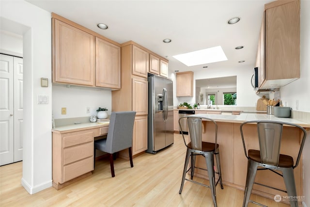 kitchen with light brown cabinetry, light hardwood / wood-style flooring, built in desk, stainless steel appliances, and kitchen peninsula