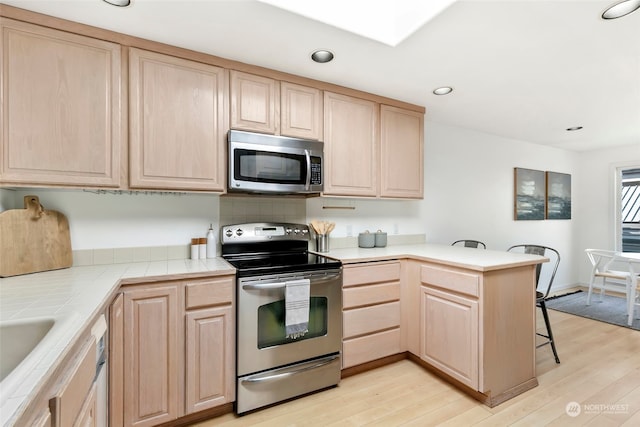 kitchen featuring kitchen peninsula, light brown cabinetry, appliances with stainless steel finishes, and light wood-type flooring