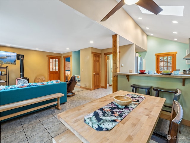 dining room with a wood stove, vaulted ceiling with skylight, ceiling fan, and light tile patterned floors