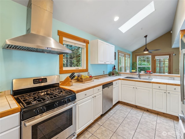 kitchen with appliances with stainless steel finishes, a healthy amount of sunlight, wall chimney exhaust hood, and tile countertops