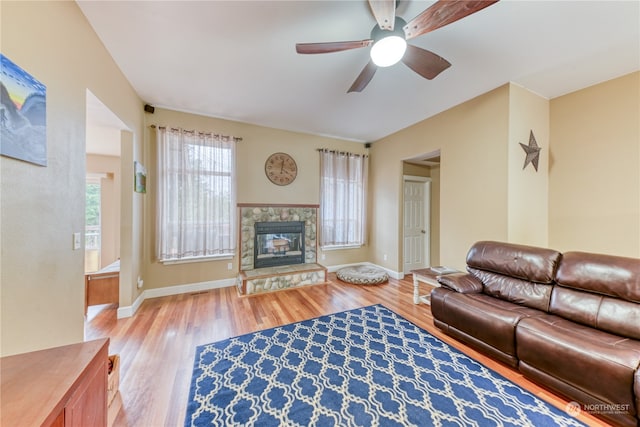 living room featuring light wood-type flooring, a stone fireplace, and ceiling fan