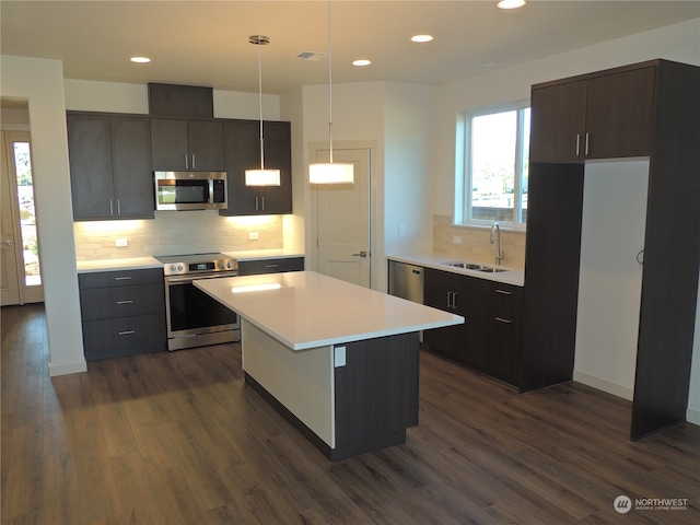 kitchen with appliances with stainless steel finishes, dark wood-type flooring, backsplash, a kitchen island, and decorative light fixtures