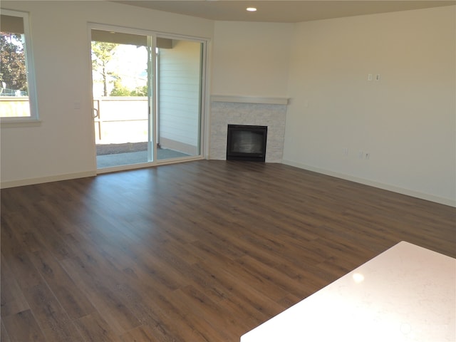 unfurnished living room with a healthy amount of sunlight, a tile fireplace, and dark wood-type flooring