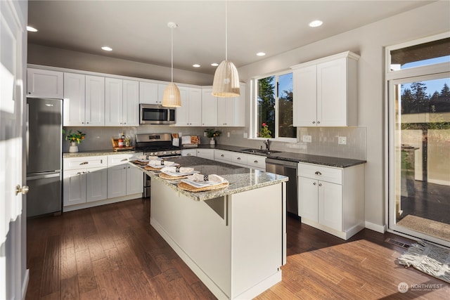 kitchen with appliances with stainless steel finishes, white cabinets, a center island, dark stone counters, and dark hardwood / wood-style floors