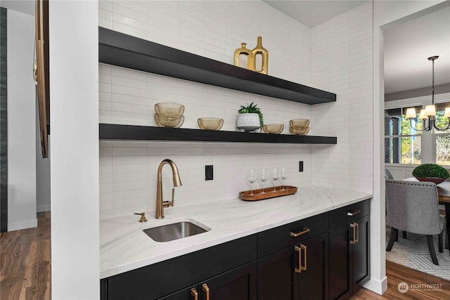 bar with hanging light fixtures, dark wood-type flooring, light stone counters, tasteful backsplash, and sink