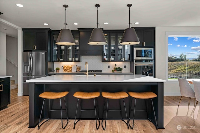 kitchen featuring light wood-type flooring, a kitchen island with sink, pendant lighting, and stainless steel appliances