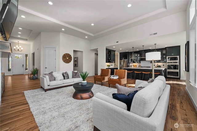 living room with a notable chandelier, a towering ceiling, a tray ceiling, and dark wood-type flooring