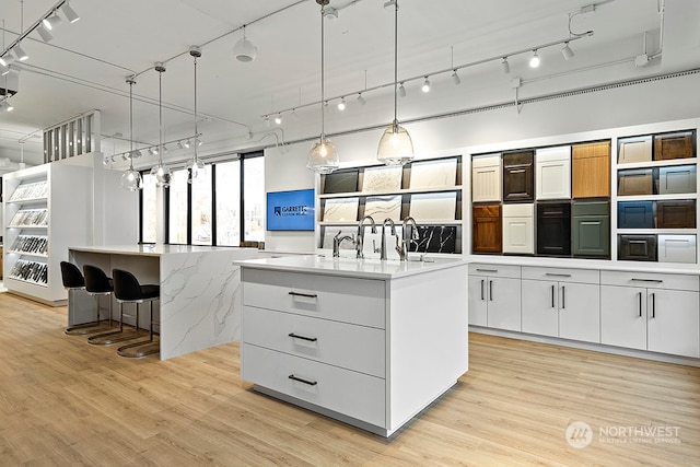 kitchen with an island with sink, hanging light fixtures, light hardwood / wood-style floors, and white cabinetry