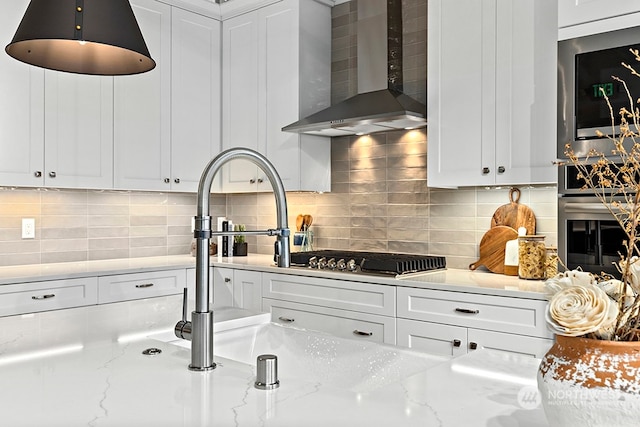 kitchen featuring wall chimney exhaust hood, white cabinets, appliances with stainless steel finishes, and tasteful backsplash